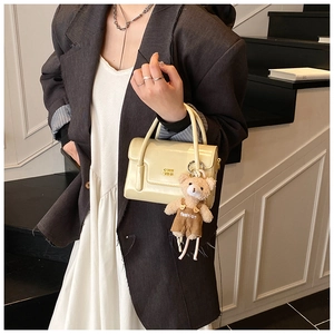 Detail of cream square handbag with cute plush bear charm and metallic brand logo