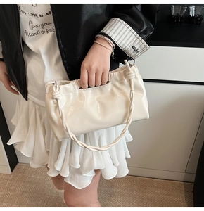 Detail of a creamy white pleated handbag featuring a twisted rope handle and glossy finish
