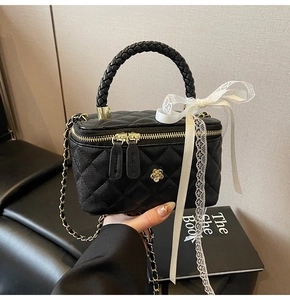 Detail of black quilted vanity bag with gold camellia clasp and white lace bow ribbon