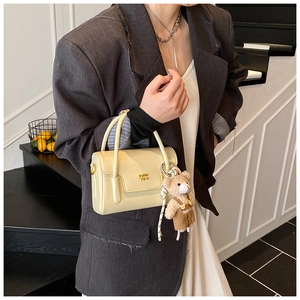 Detail of minimalist cream square bag with gold lettering and cute bear plush charm