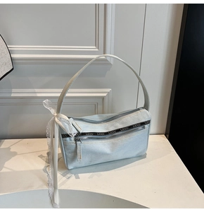 Detail of light blue denim baguette bag featuring white lace bow and metal zippers
