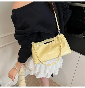 Pale yellow drawstring handbag with woven handle and metallic shoulder strap on model
