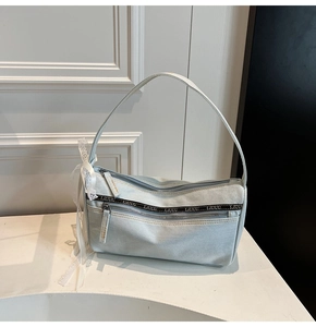 Detail of light blue denim bag featuring white lace bow and black logo strap