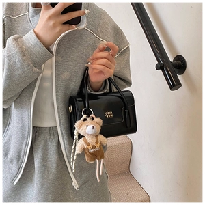 Detail of black patent leather crossbody bag with golden hardware and plush bear charm