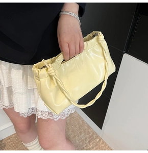 Detail of pale yellow glossy PU handbag with pleated design and woven knot handle