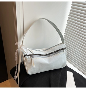 Detail of light blue denim baguette bag with dual zippers and lace bow accent