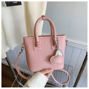 Detailaufnahme der rosa Eimer-Handtasche mit Litschi-Muster und herzförmigem Anhänger