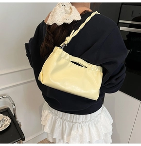 Close-up of a cream yellow pleated shoulder bag with glossy finish and knot strap detail