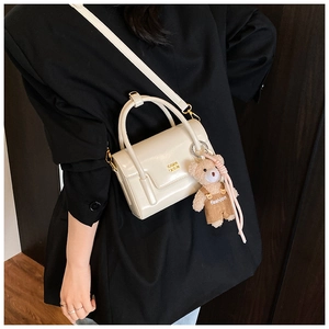 Detail of cream crossbody bag with gold chain and plush bear charm on black blazer