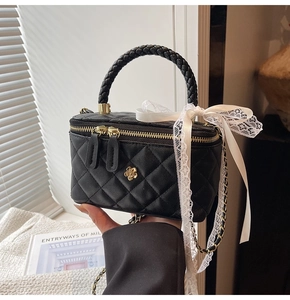 Detail of black quilted leather box bag with golden camellia badge and woven handle