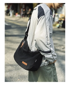 Macro detail of the black nylon messenger bag featuring leather brand logo and silver zipper