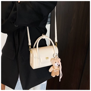 Detail of off-white leather crossbody bag with gold metal logo and brown teddy bear pendant