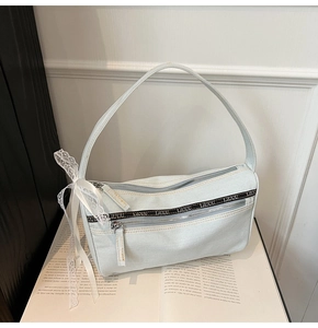 Detail of light blue denim baguette bag with lace trim and silver zippers on a magazine