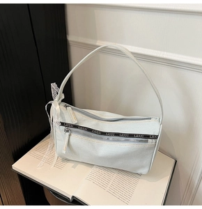 Detail of light blue denim baguette bag with double front zippers and lace bow charm