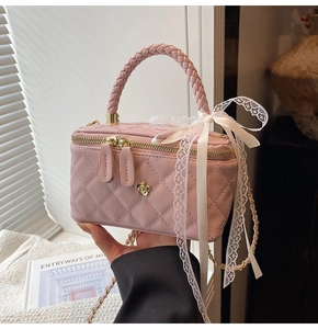Detail of pink quilted leather vanity bag featuring a gold camellia and woven handle