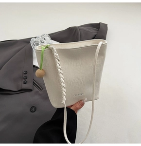 Detail view of cream bucket bag showing lychee grain texture and green drawstring charm