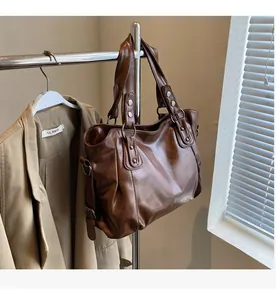 Detailed view of a vintage brown leather tote bag with rivets hanging on a metal rack
