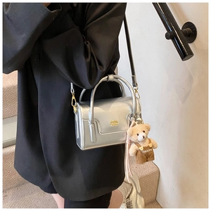 Close-up of metallic silver mini square bag with golden logo and cute plush bear charm