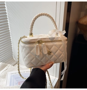 Detail view of white quilted box bag with camellia ornament and woven leather handle