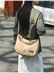 Outdoor shot showing a woman wearing a beige nylon crescent crossbody bag with strap details