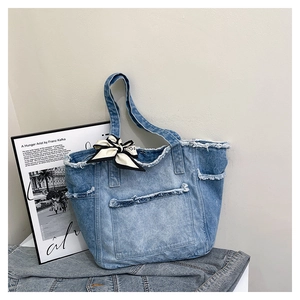 Détail du sac cabas en denim lavé avec bords effilochés et ruban de décoration à nœud