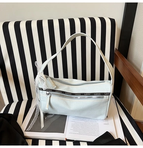 Close-up of light blue denim baguette bag with metal zippers and lace bow on a book