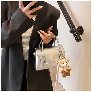 Detail of a silver metallic square bag with a cute teddy bear charm and fashion logo