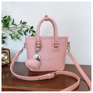 Detail der rosa Handtasche mit Herzanhänger und Metallkette auf einer Holzoberfläche