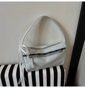 Detail of light blue denim baguette bag with silver double zippers and lace bow