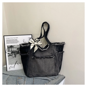 Détail du sac cabas en jean avec un nœud en ruban blanc et des bords effilochés