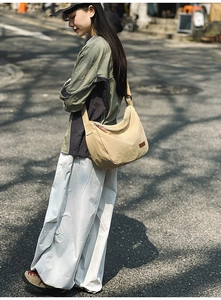 Close-up of a beige crescent nylon crossbody bag worn on a street with a leather logo tag
