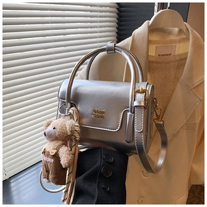 Detailed shot of a metallic silver handbag with a gold logo and a cute plush bear charm