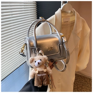 Detail of silver metallic handbag with plush bear charm and adjustable shoulder strap
