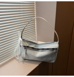 Detail of light blue denim baguette bag with double zippers and white lace bow accessory