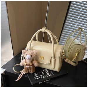 Detail of cream square handbag with gold logo, round handles and cute plush bear charm