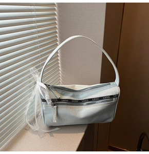 Detail of light blue denim baguette bag featuring white lace bows and double zippers