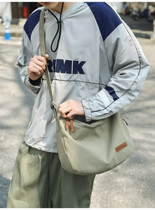Close-up of sage green nylon dumpling bag showing adjustable strap and brown leather logo patch