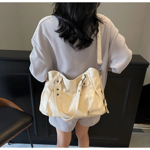 Detail of cream-colored oversized tote bag with rivets and dual handles on a female model