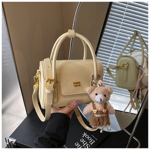 Detail of cream PU leather crossbody bag with metal logo, shoulder strap and bear charm
