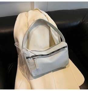 Close-up of white denim baguette bag featuring metal zippers and lace bow detail