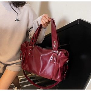 Close-up of deep red leather tote bag with silver rings and rivet details in hand