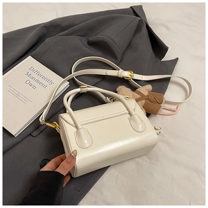 Detail of cream square handbag with gold hardware, plush bear charm, and shoulder strap