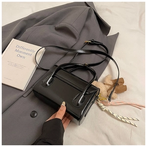 Minimalist black square bag on a grey suit with a cute bear charm and golden hardware
