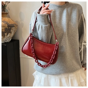 Detail of a dark red glossy underarm bag featuring a decorative matching thick chain strap