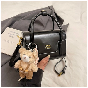 Close-up of black glossy patent leather crossbody bag with a cute teddy bear charm