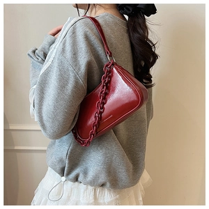 Detail of red patent leather baguette bag with thick chain strap worn by a model