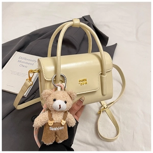 Detail of cream rectangular handbag with golden logo and cute teddy bear charm on grey blazer