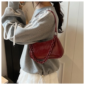 Detail of dark red glossy underarm bag with a matching chunky resin chain and leather strap