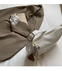 Gros plan d'un sac à bandoulière en PU blanc brillant avec détails dorés et breloque