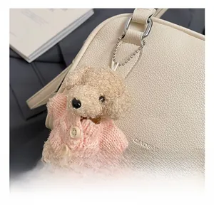 Detail of plush poodle charm with pink knit sweater on a textured leather handbag